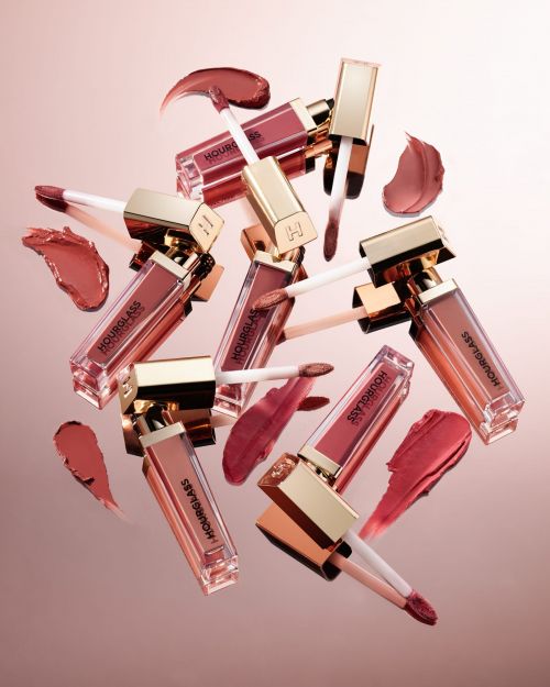 Close-up shot of multiple Hourglass brand lip gloss tubes with gold lids and clear containers, displayed with matching color swatches.