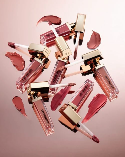 Close-up shot of multiple Hourglass brand lip gloss tubes with gold lids and clear containers, displayed with matching color swatches.