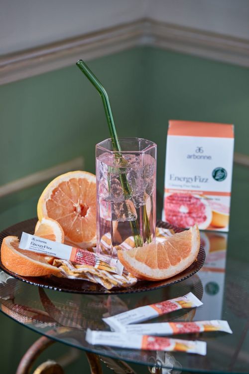 Drink with grapefruit and lemon, including a green straw in a clear glass, surrounded by additional citrus and product packaging.