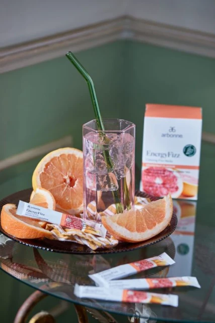 Drink with grapefruit and lemon, including a green straw in a clear glass, surrounded by additional citrus and product packaging.