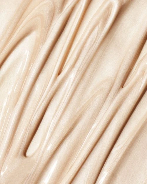 Close-up shot of a shiny, light beige cream, swirled and rippled to display its smooth, thick texture, and light-reflecting qualities.