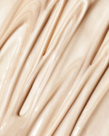 Close-up shot of a shiny, light beige cream, swirled and rippled to display its smooth, thick texture, and light-reflecting qualities.