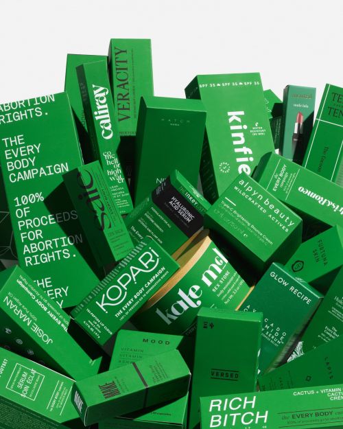 Pile of green cosmetic product packaging with various brand names and product information labels in a studio setting.