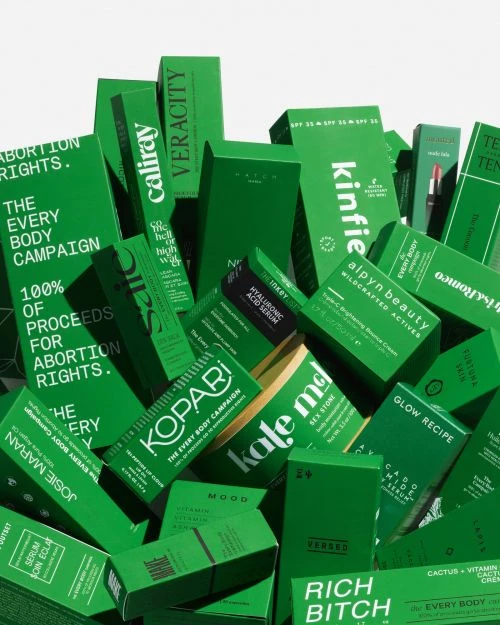 Pile of green cosmetic product packaging with various brand names and product information labels in a studio setting.