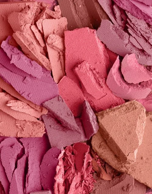 Close-up of smashed eyeshadow palette with a mix of pink, coral, and mauve hues creating an abstract pattern and textured surface.