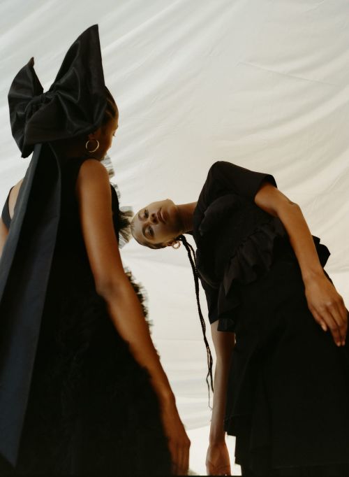 Two models in black dresses with large bows against a draped white backdrop styled by Leah Adicoff