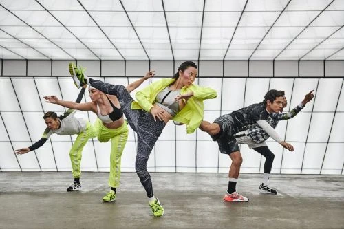 Four athletic adults in neon activewear strike dynamic poses in a bright studio with a geometrically patterned white ceiling and gray floor.