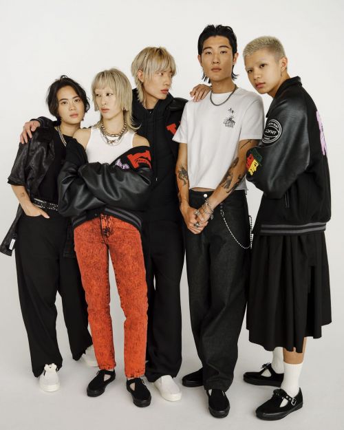 A group of five young adults of diverse ethnicities pose together in an eye-level studio shot against a white backdrop, showcasing street fashion.