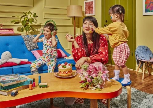 Indoor shot of a mother with two young children. The little girl is putting make-up on her mother's face with the boy dancing with headphones.