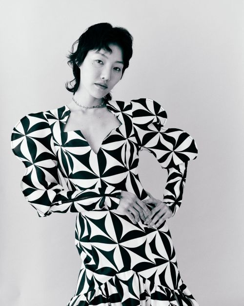 Portrait of an Asian woman wearing a black-and-white geometric patterned dress against a neutral backdrop. Fashion and studio lighting.