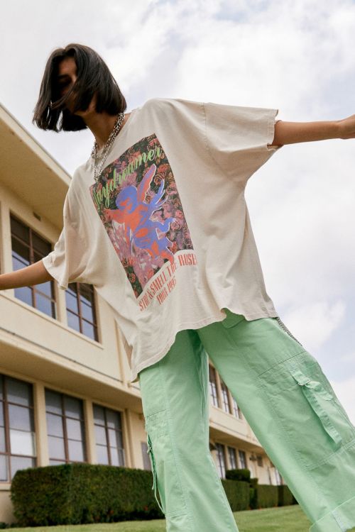 Woman wearing a white t-shirt with graphic and mint-green cargo pants stands outside a light-beige building on a sunny day.