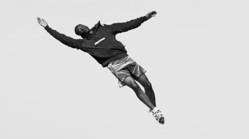 An African American man in athletic wear suspended mid-air against a bright backdrop, seemingly floating or in a dynamic jump pose.