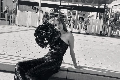 Woman in sequined one-shoulder jumpsuit holding a large decorative rose sculpture in Los Angeles.