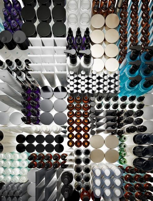 Overhead shot displaying neatly organized beauty and cosmetic products in various containers: bottles, jars, tubes in clear and solid colors.
