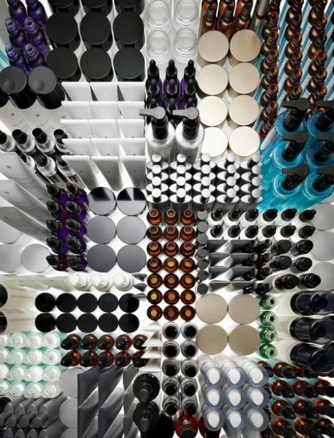 Overhead shot displaying neatly organized beauty and cosmetic products in various containers: bottles, jars, tubes in clear and solid colors.