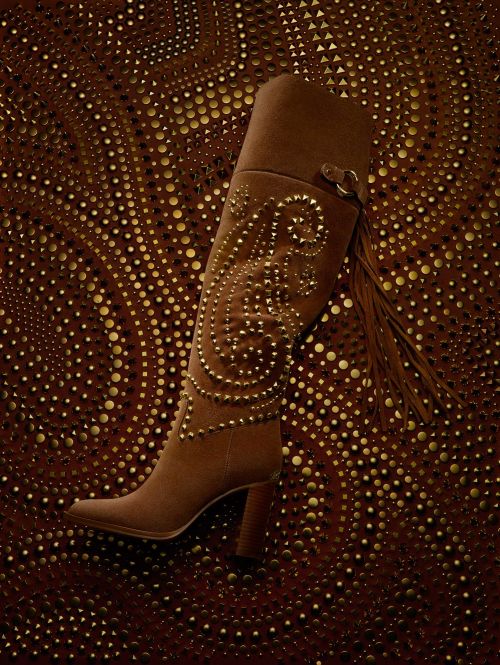 Brown suede knee-high boot with gold studs on a textured brown and gold background. Fashionable women's footwear, stylish design.