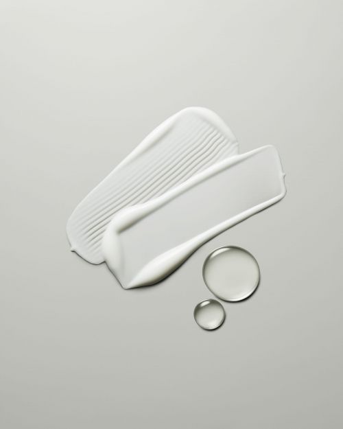 Close-up shot of two textured cream smears and two translucent liquid drops on a gray background.