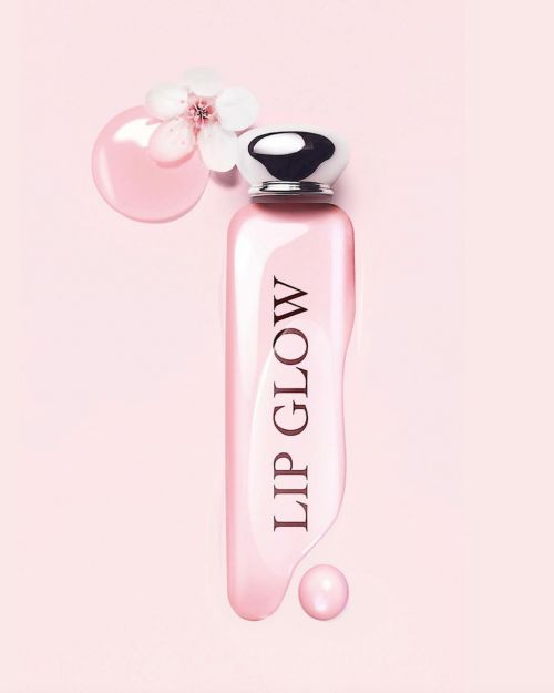 Pink cosmetic bottle with silver cap displaying lip glow text surrounded by liquid pink gloss and white flower