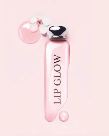 Pink cosmetic bottle with silver cap displaying lip glow text surrounded by liquid pink gloss and white flower