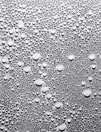 A macro photograph captures countless water droplets of varying sizes scattered across a smooth, silvery metallic surface, creating a textured effect.