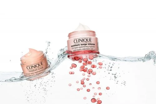 Two jars of Clinique Moisture Surge Intense skin cream stand partially submerged in clear water with coral-colored droplets on white.