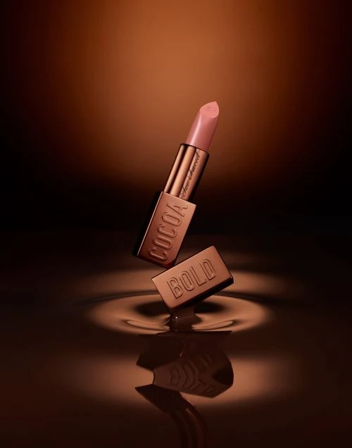 Elevated view of a Cocoa Bold lipstick tube, with the cap slightly separated and a chocolate ripple effect at the base.