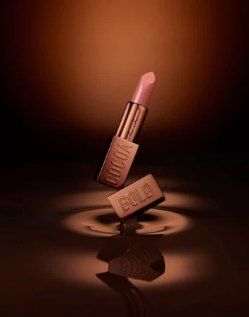 Elevated view of a Cocoa Bold lipstick tube, with the cap slightly separated and a chocolate ripple effect at the base.