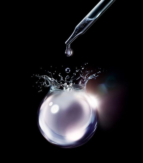 Close-up shot of a clear liquid droplet falling from a pipette into a translucent sphere with a splash against a dark backdrop.