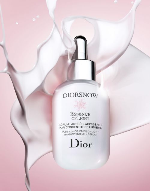 Dior serum bottle presented against a backdrop of milk splashes and a soft pink gradient, ideal for beauty and skincare advertising.