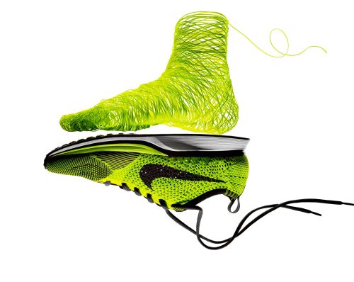 Studio shot of a bright neon green and black running shoe next to a sculptural yarn form of a foot on a white background.