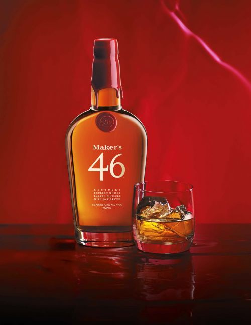 Maker's 46 Kentucky bourbon whiskey bottle next to a glass of whiskey with ice against a red background, studio shot.