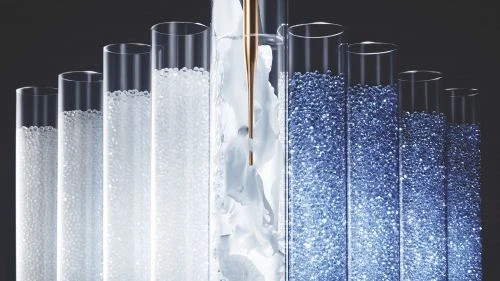 Test tubes with white and blue beads and a gold metal dropper on a dark gray background in a laboratory-themed still-life image.