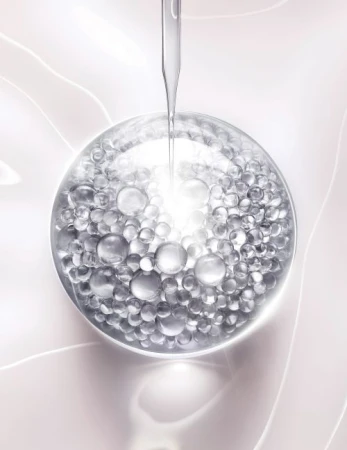 Close-up of clear serum droplet falling onto a translucent sphere filled with smaller silver beads against a pale pink background.