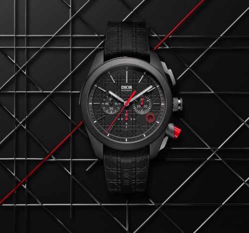 Luxury black wristwatch with red accents on a matching strap displayed on a dark geometric surface for a high-end fashion advertisement.