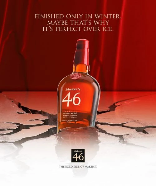 Maker's 46 bourbon bottle stands on cracked surface against a red backdrop. Advertising promotes winter finishing and serving over ice.