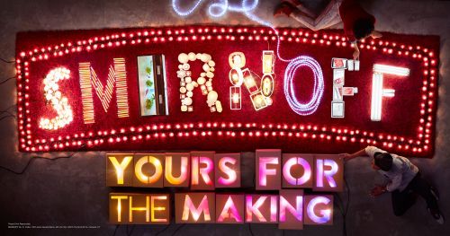 Overhead shot of two adults setting up illuminated letter boxes, spelling 'YOURS FOR THE MAKING' below a neon sign.