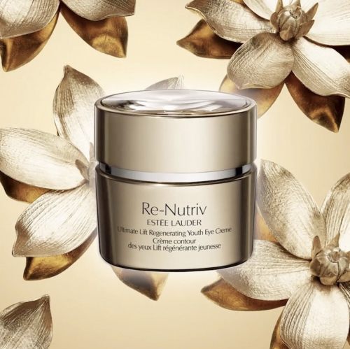 Close-up of Estee Lauder Re-Nutriv eye creme jar on a tan background with gold floral decorations, product shot for beauty advertising.
