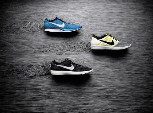 Three Nike running shoes are displayed in a studio setting with a textured dark background. The shoes are in black, blue, and gray.