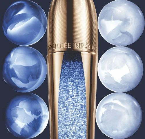 Orchidée Impériale gold and blue skincare product with round shimmering orbs against a dark background in a studio shot.