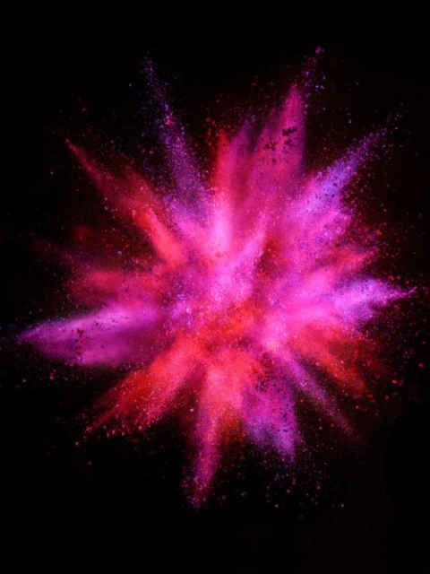 A colorful explosion of magenta, pink, and red powder against a dark background, creating an abstract burst of color and energy.