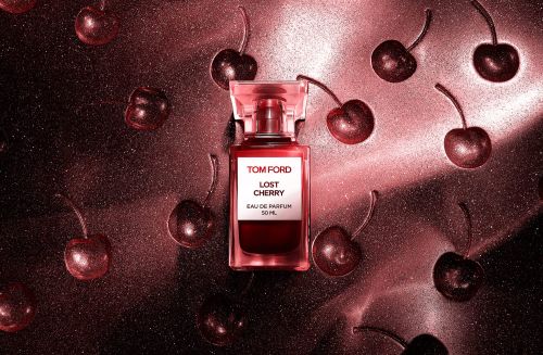 Tom Ford Lost Cherry perfume bottle surrounded by glossy dark cherries on a metallic pink textured background.