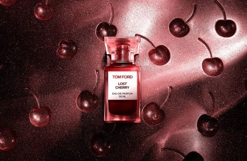 Tom Ford Lost Cherry perfume bottle surrounded by glossy dark cherries on a metallic pink textured background.