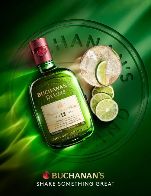 Buchanan's Deluxe whiskey bottle with a red cap, a glass of clear liquid with ice, and lime slices against a green background.