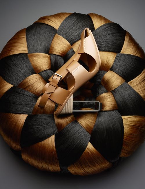 Fashion sandal resting atop a textural woven disc made of black and tan hair. Studio lit fashion product photography.