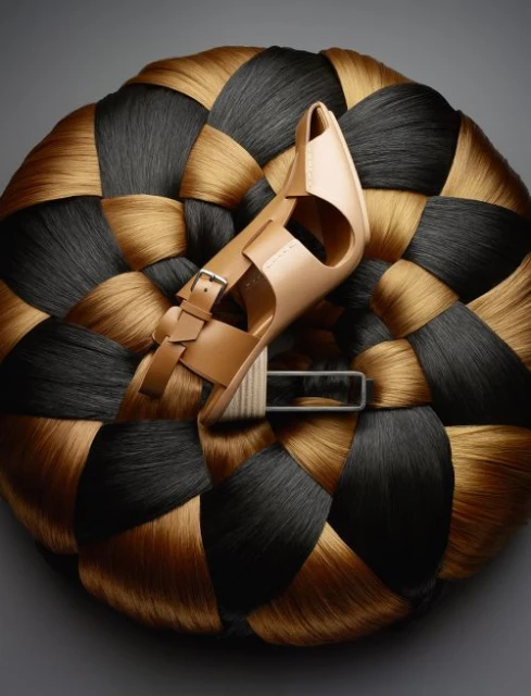 Fashion sandal resting atop a textural woven disc made of black and tan hair. Studio lit fashion product photography.