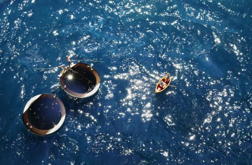 Aerial view of a small boat with people on a sparkling blue body of water, next to two floating platforms with solar panels.