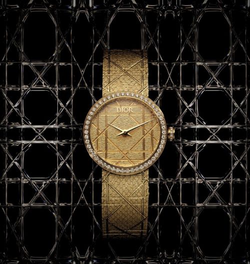 Elegant gold Dior watch with diamond bezel and patterned strap displayed against a textured black background; a luxurious timepiece.