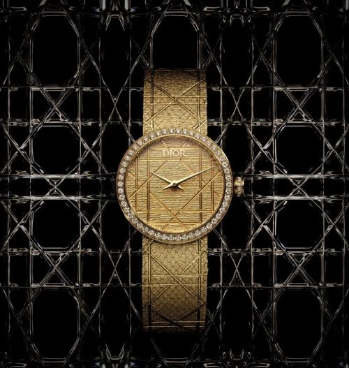 Elegant gold Dior watch with diamond bezel and patterned strap displayed against a textured black background; a luxurious timepiece.