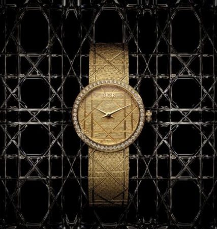 Elegant gold Dior watch with diamond bezel and patterned strap displayed against a textured black background; a luxurious timepiece.