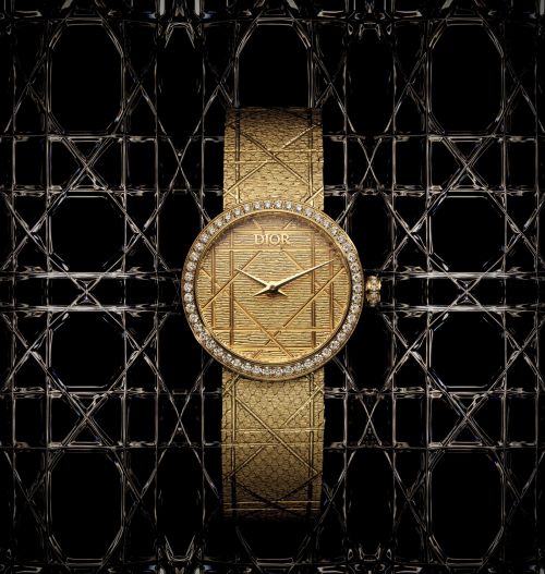 Elegant gold Dior watch with diamond bezel and textured strap set against a geometric, lattice-like black and silver background.